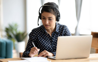 Focused Indian Girl Wearing Headset Writing Notes, Studying Onli